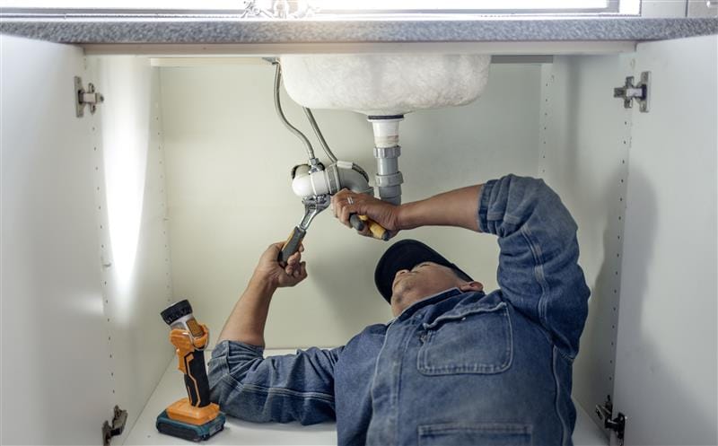 Plumber repairing pipes beneath a bathroom sink in Hemet