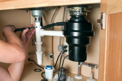 Plumber repairing a garbage disposal beneath a kitchen sink in Hemet