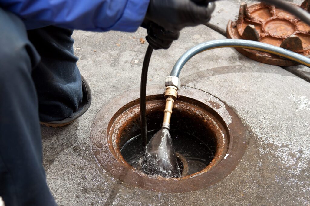 Plumber hydro jetting a sewer line through a manhole in Hemet