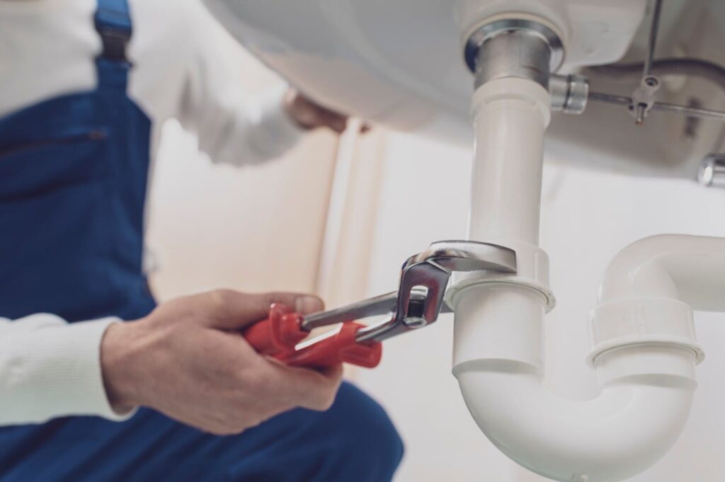 Plumber repairing a white drain pipe beneath a sink in Hemet