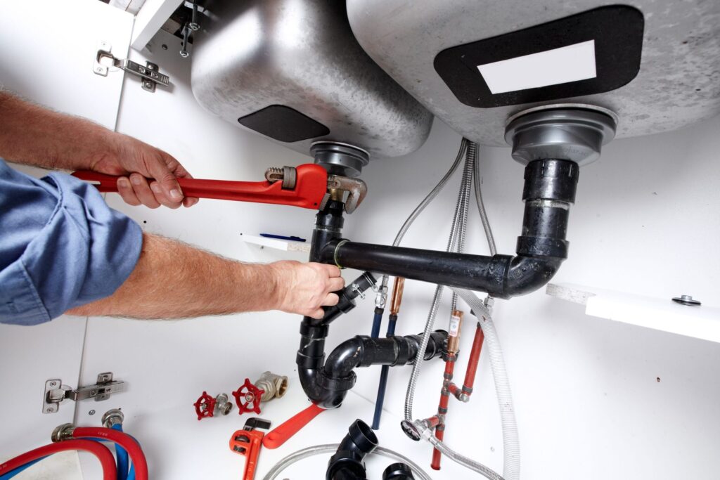 Plumber repairing drain pipes beneath a kitchen sink in Hemet